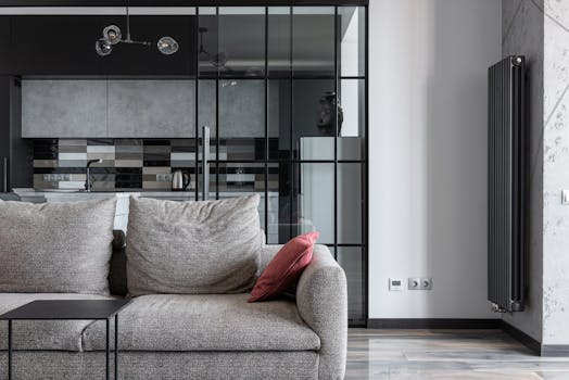 Contemporary living space featuring a stylish gray sofa, red cushion, and a view into a modern kitchen.